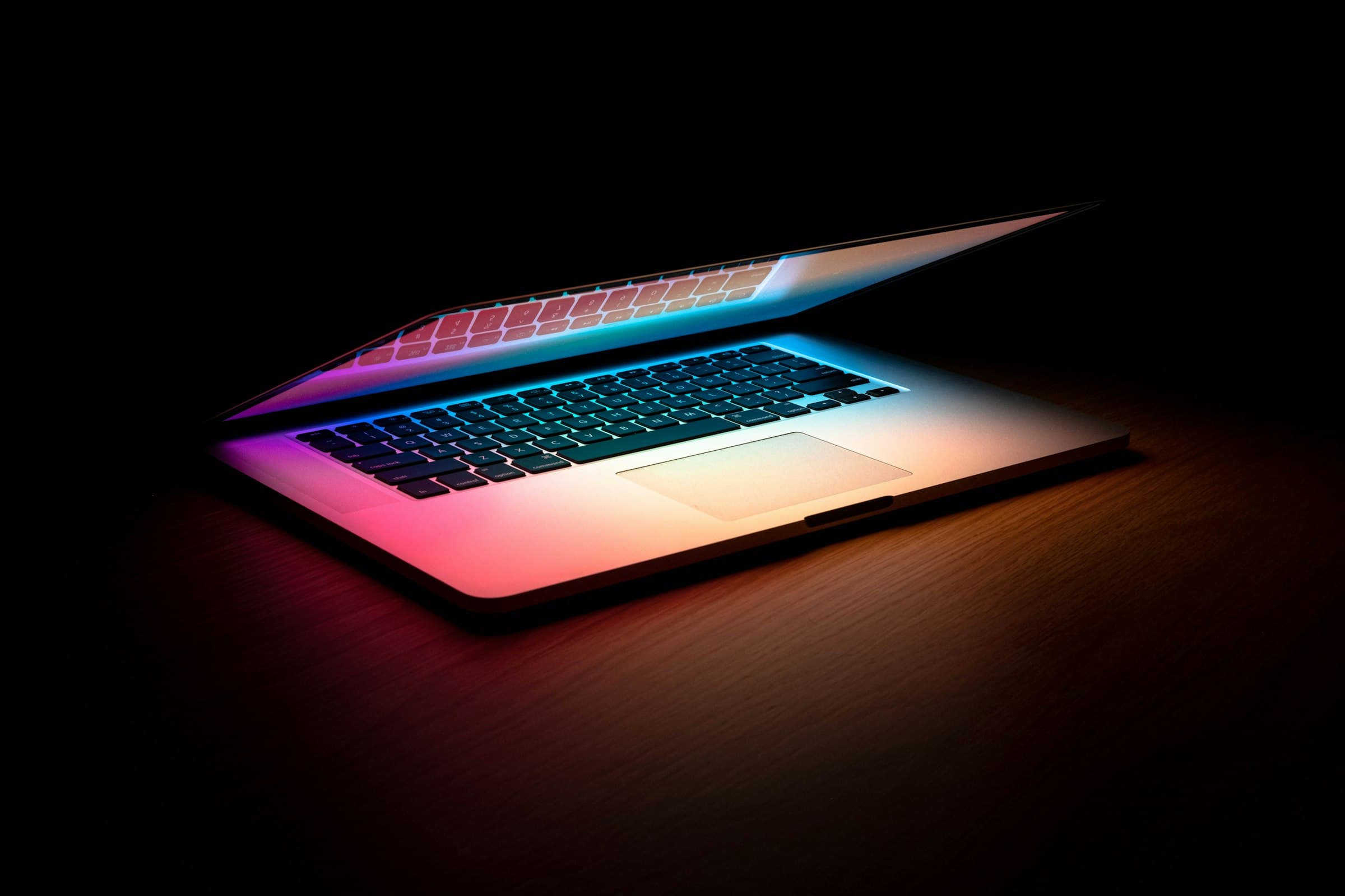A MacBook Air glowing with rainbow light on a wooden desk